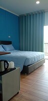 A bedroom with a bed, a bedside table with a kettle, and a curtain.