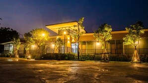 A modern building with a flat roof and large windows, surrounded by trees and a paved area. - JC Resort (Trakan Phuet Phon)
