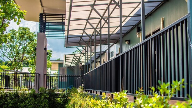 A modern building with a covered walkway, metal railings, and greenery. - JC Resort (Trakan Phuet Phon)
