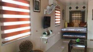 A living room with a sofa, a TV, a fan, and a decorative wall piece. - Evangeline Garden and Lodge (Silang)