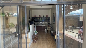 A modern kitchen with dark cabinets, a dining area with a wooden table and chairs, and a view of a parked car outside. - Evangeline Garden and Lodge (Silang)