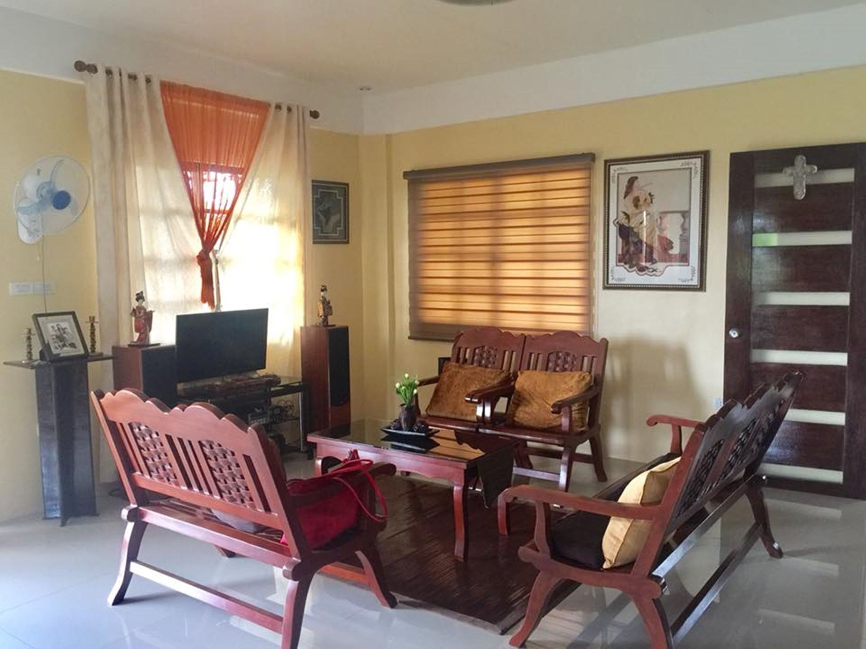 A living room with a TV, wooden furniture, a fan, and a door with a cross.