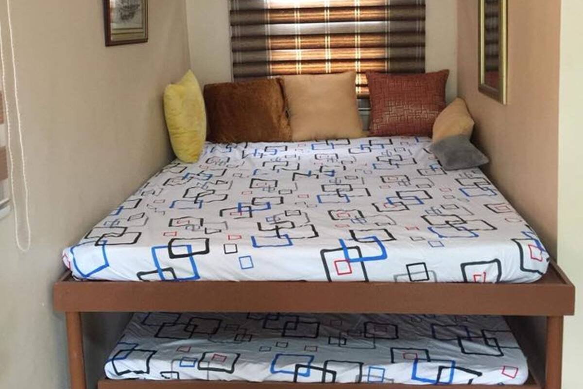 Ein kleines, gemütliches Schlafzimmer mit Bett, Kissen und einem Fenster mit Jalousien.