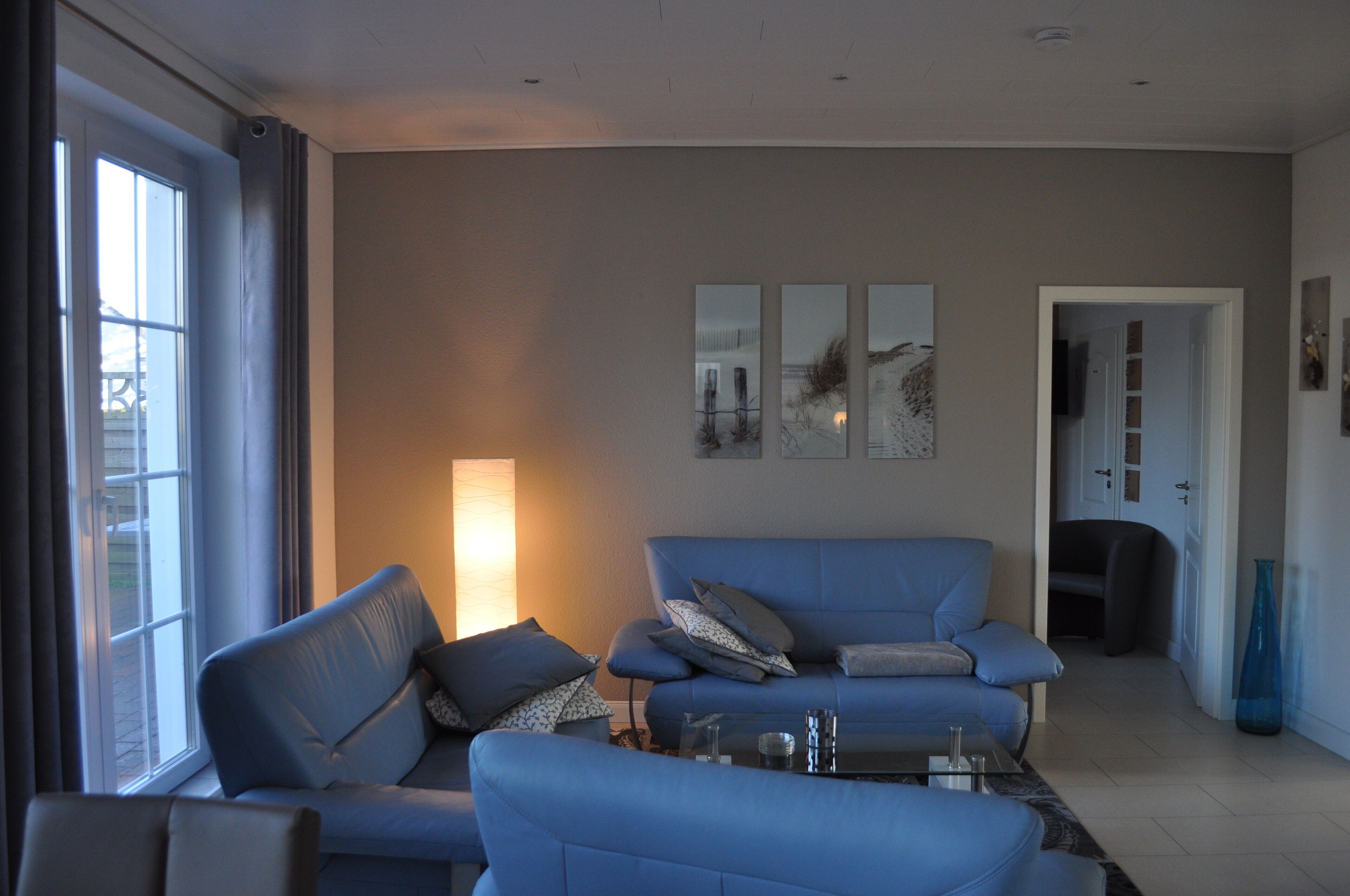 A modern living room with a blue sofa set, a coffee table, and a large window with curtains.