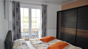 Een tweepersoonsbed met gestreept beddengoed en twee oranje kussens, een donker houten hoofdbord en uitzicht op een terras met stoelen en een tafel.