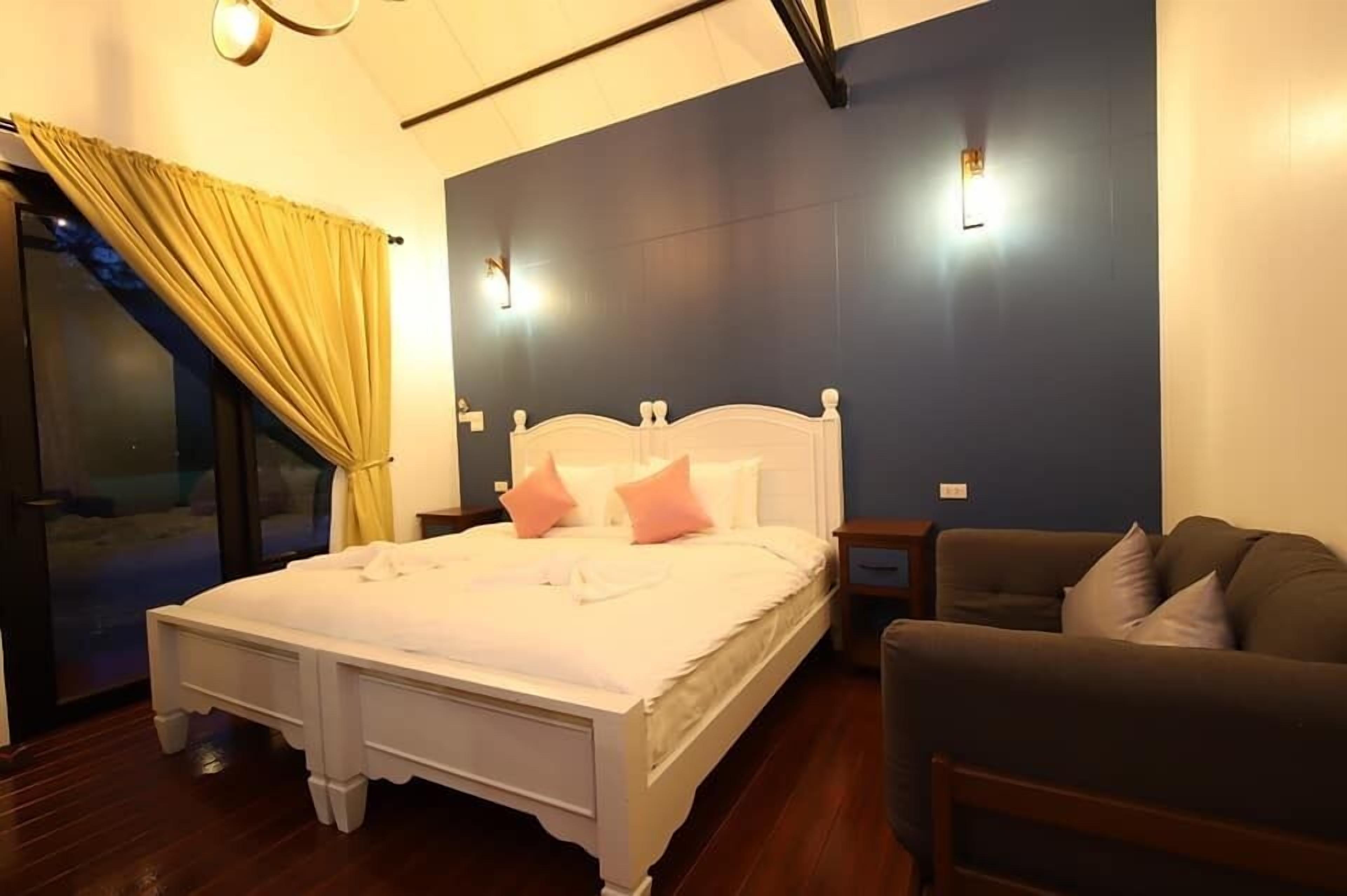 A bedroom with a bed, a sofa, and a window with curtains.
