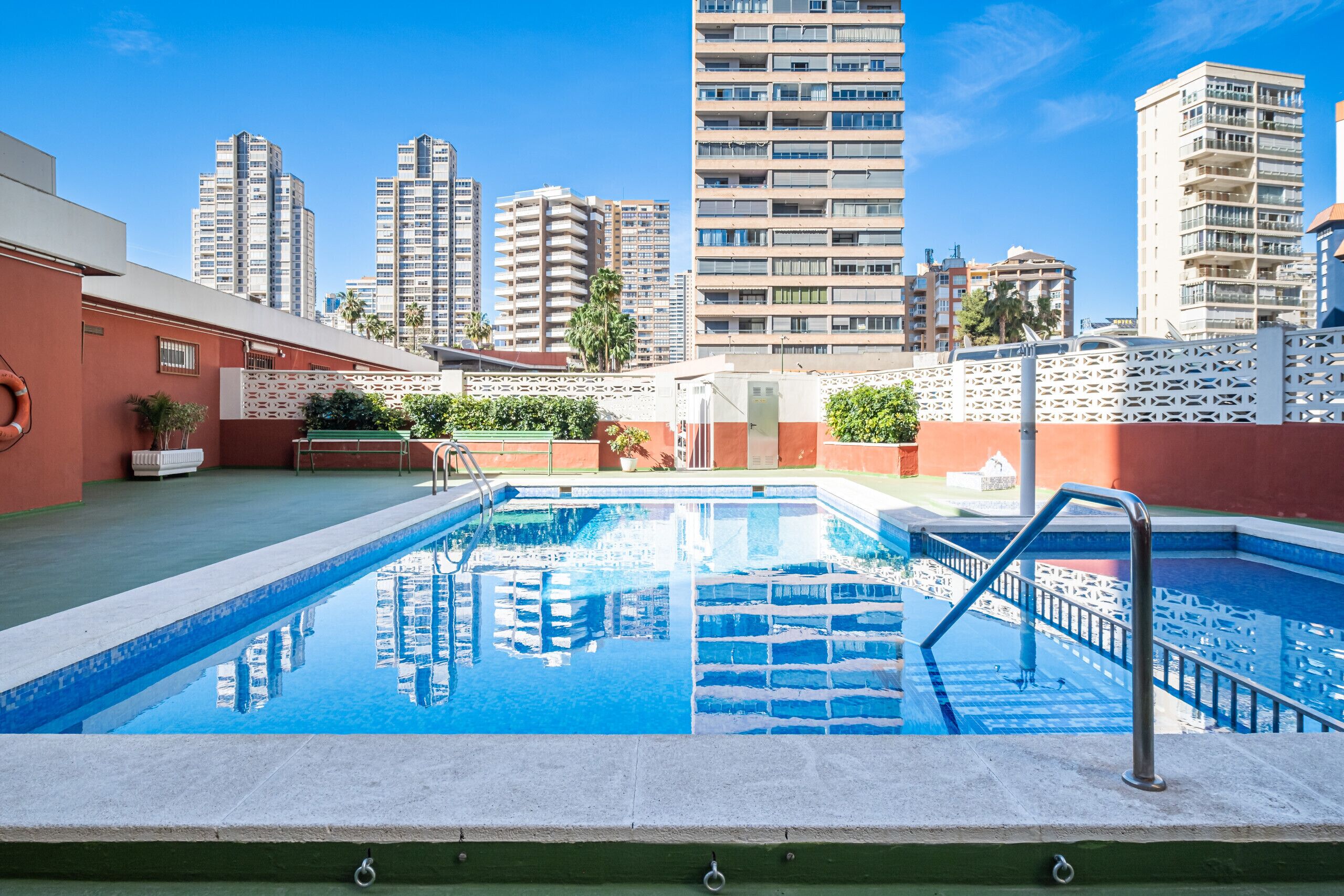 A rooftop swimming pool with a view of tall residential buildings in the background.