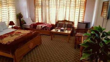 Quarto de hotel com uma cama, um sofá, uma mesa pequena e uma cadeira. Há uma planta em vaso no canto.