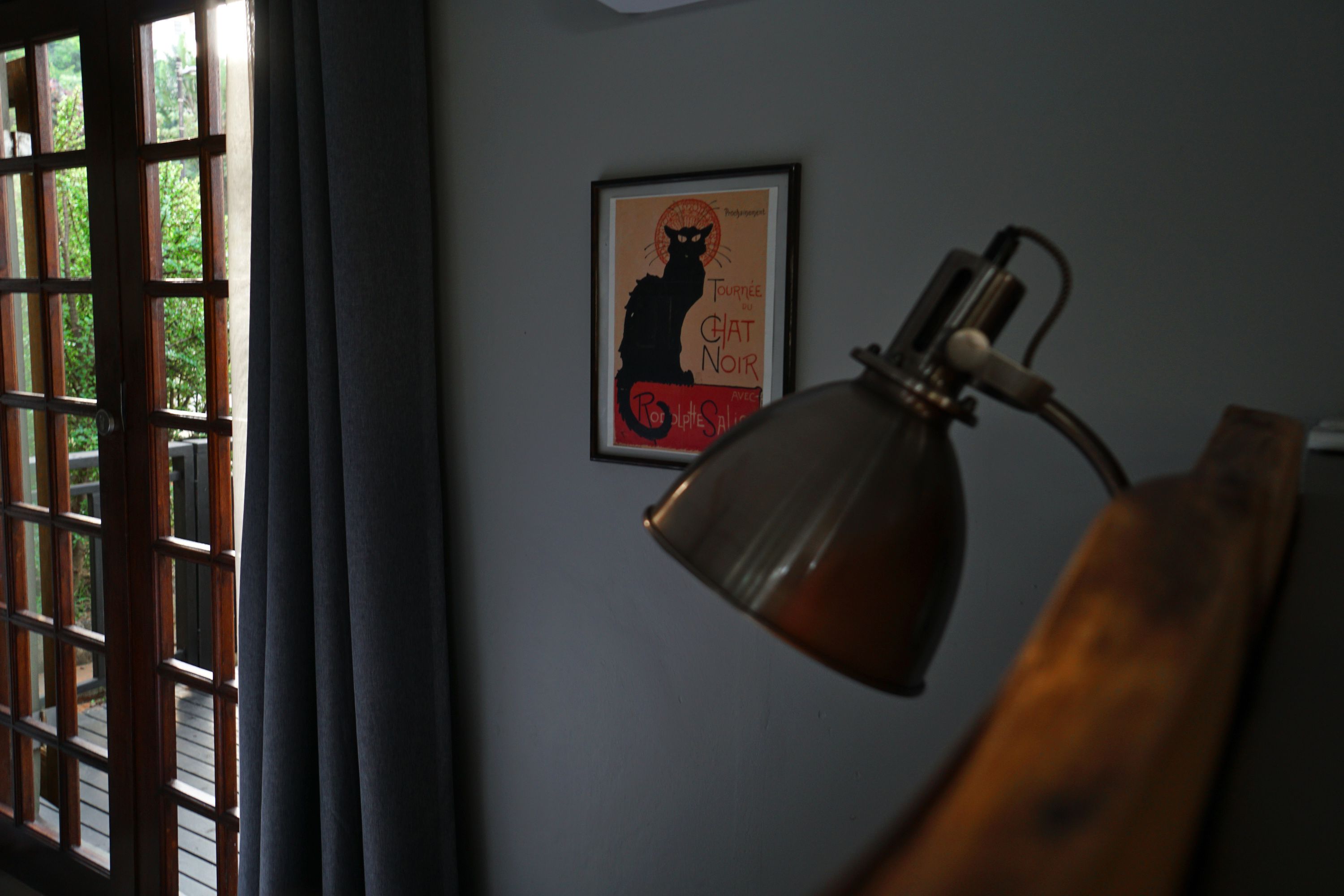 Una habitación con ventana, un cartel enmarcado en la pared y una lámpara de escritorio.