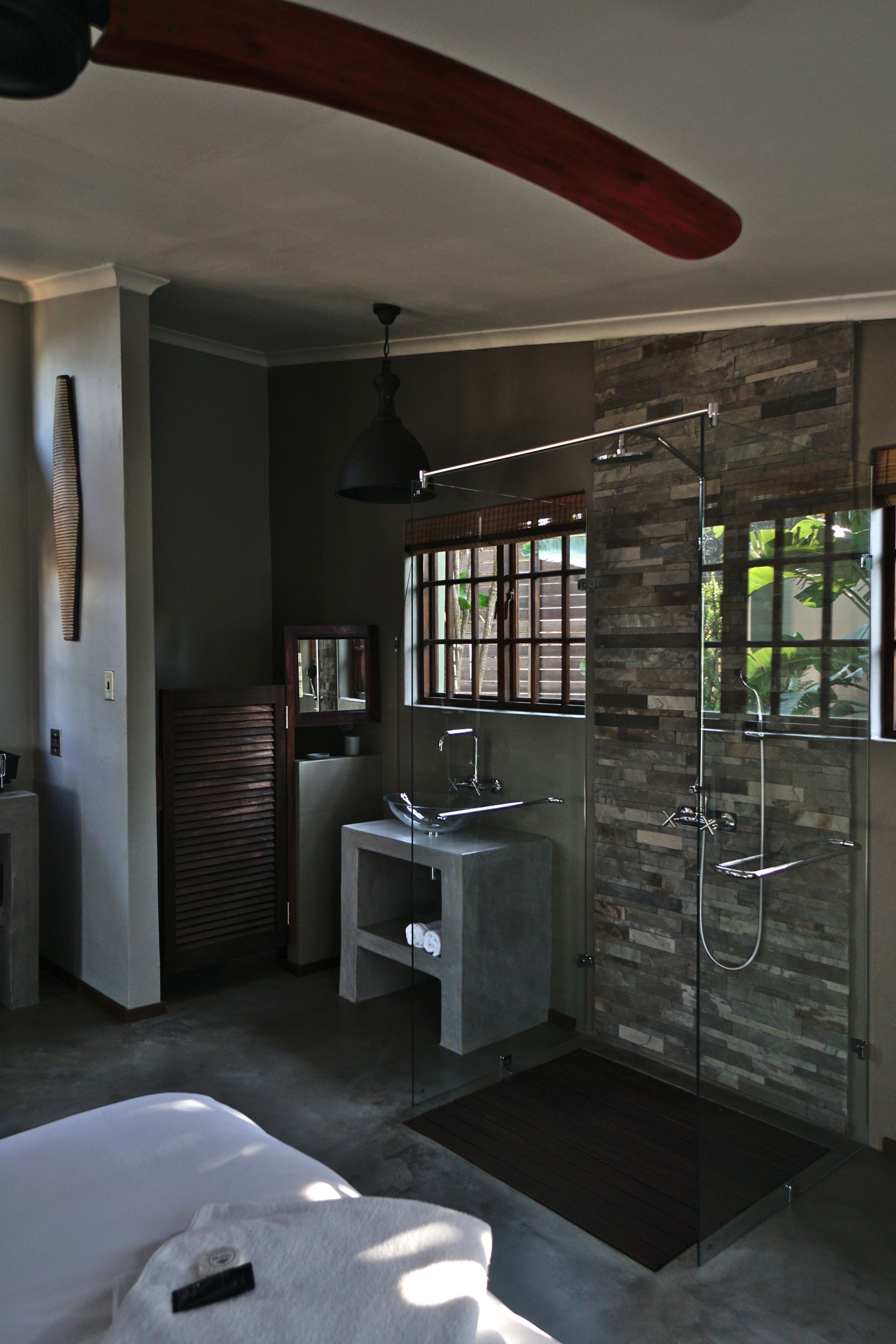 Un baño moderno con pared de piedra, cabina de ducha de vidrio y lavamanos empotrado.