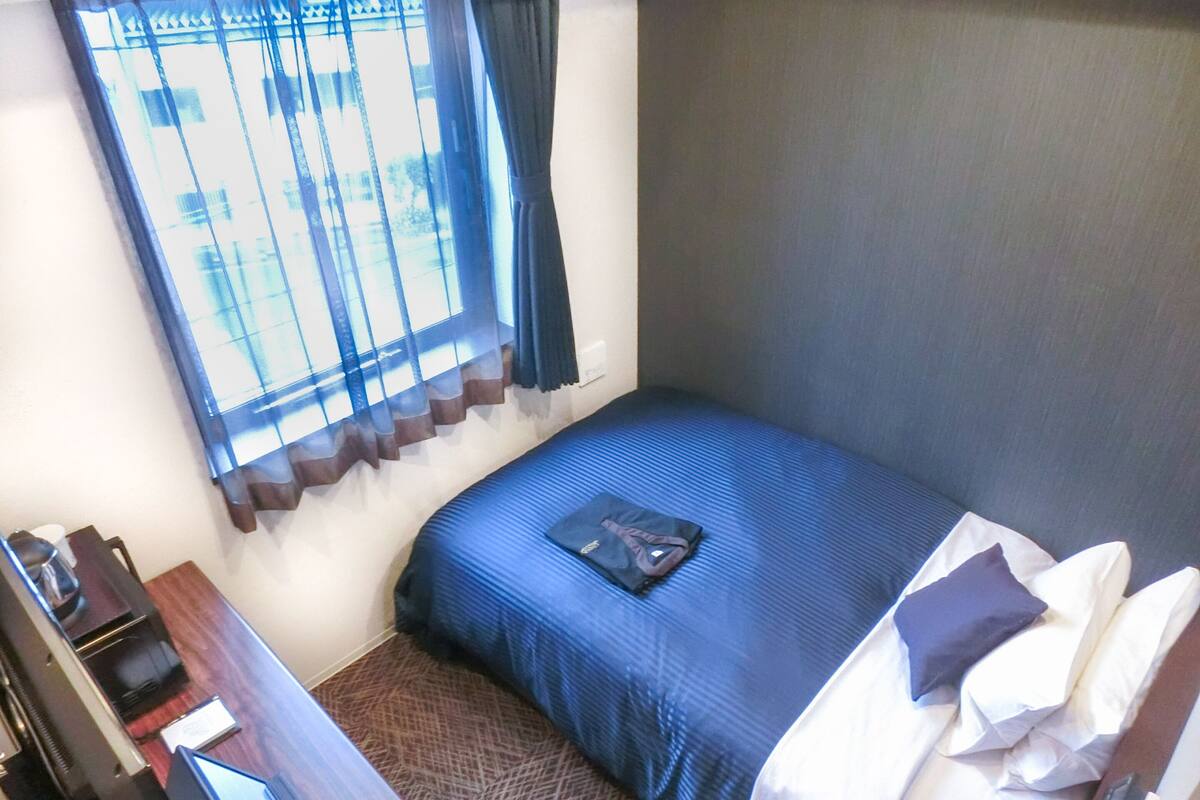 Une petite chambre à coucher, bien rangée, avec un lit simple, un bureau et une chaise.