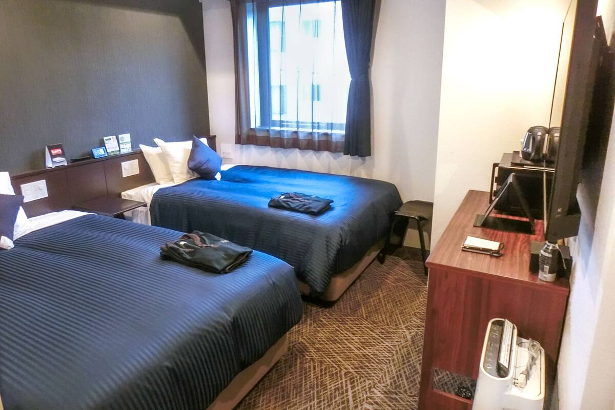 Une chambre d’hôtel avec deux lits, un bureau, une télévision et une fenêtre avec des rideaux.