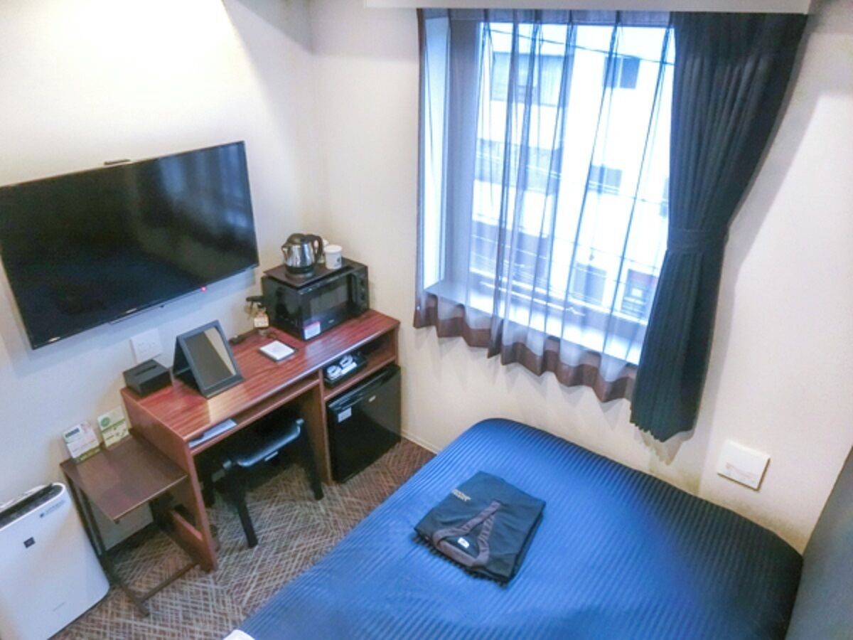 Ein Hotelzimmer mit Bett, Schreibtisch mit Computer, Fernseher und einem Fenster mit Vorhängen.