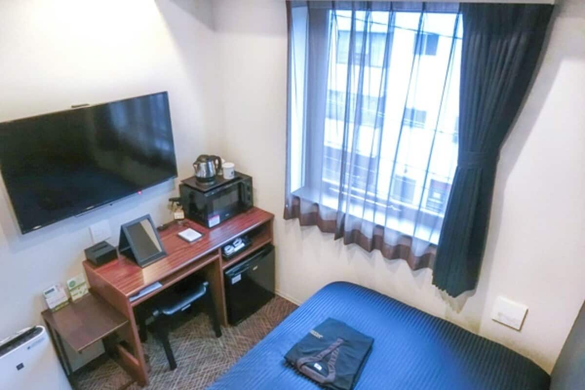 A hotel room with a bed, a desk with a computer, a television, and a window with curtains.