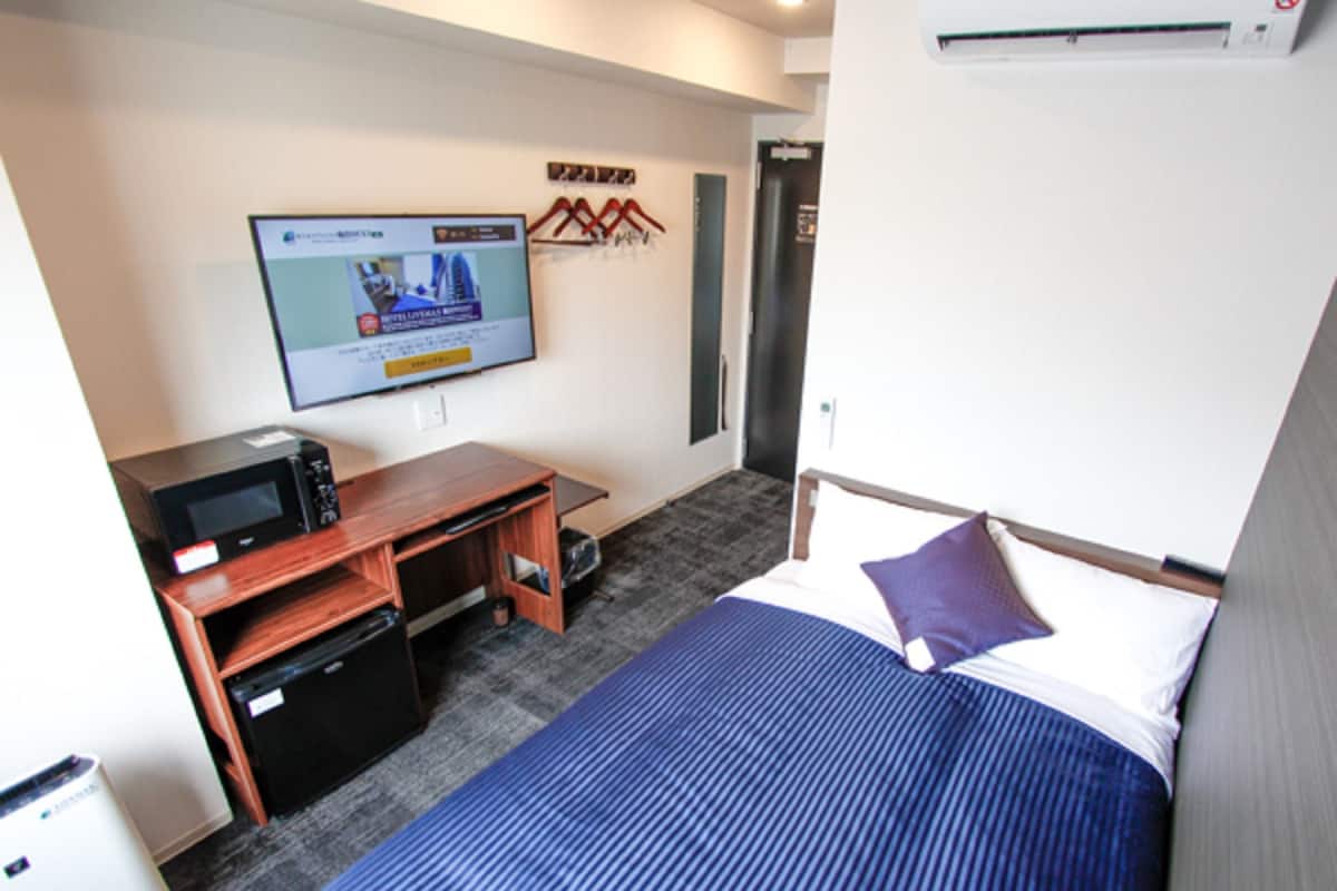 Una habitación de hotel con cama, escritorio, microondas y televisión en la pared.