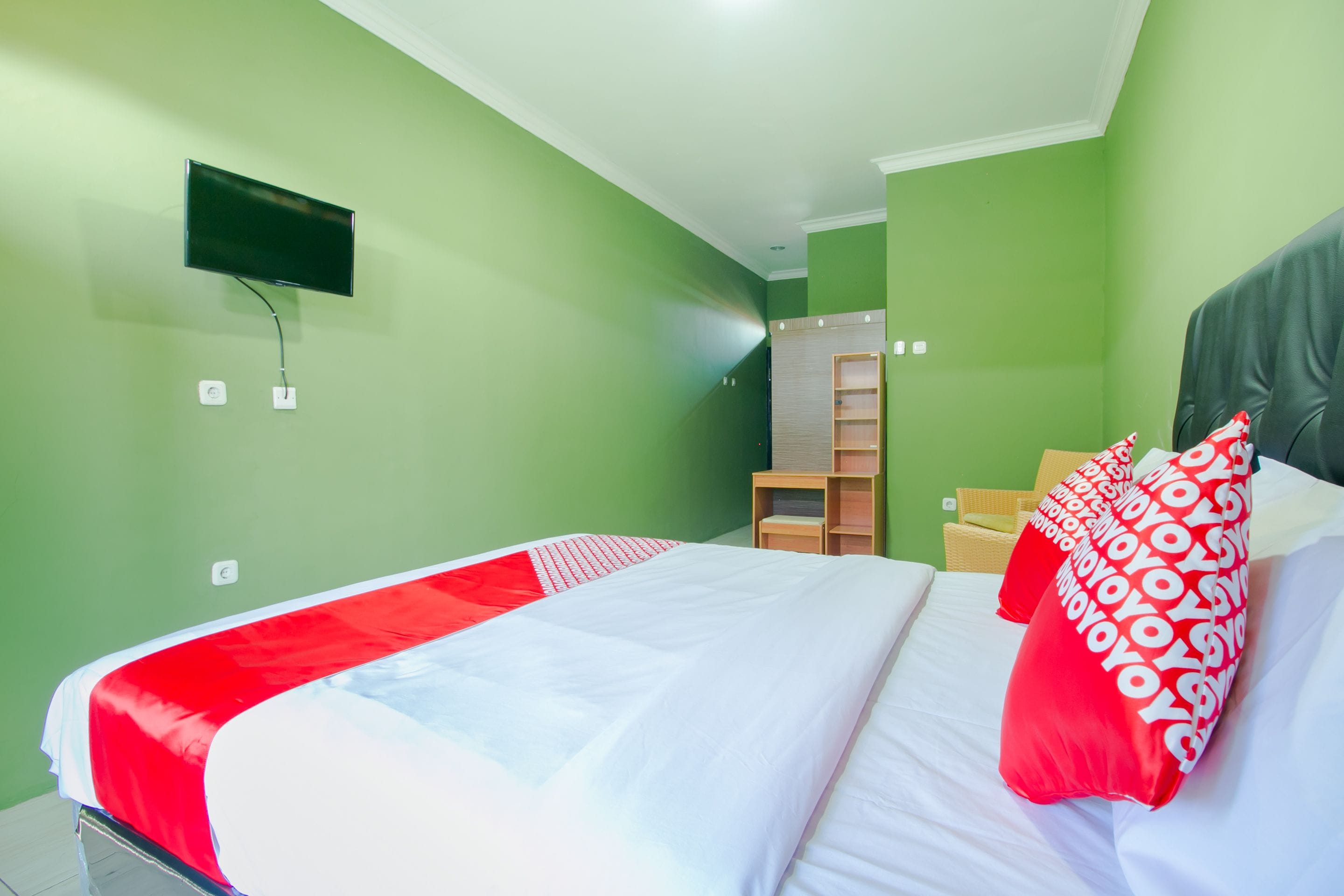 Una habitación de hotel con cama, televisor montado en la pared y armario de madera.