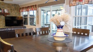 A dining area with a wooden table, chairs, a vase with dried flowers, and a television on a stone wall. - FREE USE OF OUR 2022 23’ TRITOON EVERY RENTAL DAY
May 1st- Oct 31st (Albemarle)
