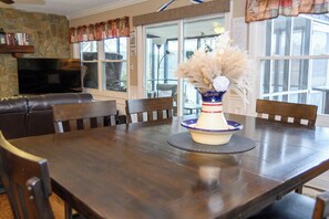 A dining area with a wooden table, chairs, a vase with dried flowers, and a television on a stone wall. - FREE USE OF OUR 2022 23’ TRITOON EVERY RENTAL DAY
May 1st- Oct 31st (Albemarle)