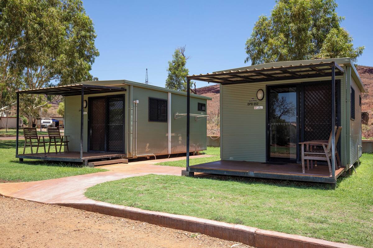 Two green mobile homes with attached porches, one with a door and the other with a window.