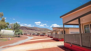 A row of single-story cabins with a covered walkway, set against a hilly backdrop. - Tom Price Tourist Park (Tom Price)