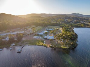 An aerial view of a coastal property with a dock, boats, and a large building complex surrounded by greenery and hills.