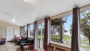A spacious room with a large wooden dining table, several chairs, a sofa, and a view of a lake through large windows. - Walpole Rest Point Caravan Park (Walpole)