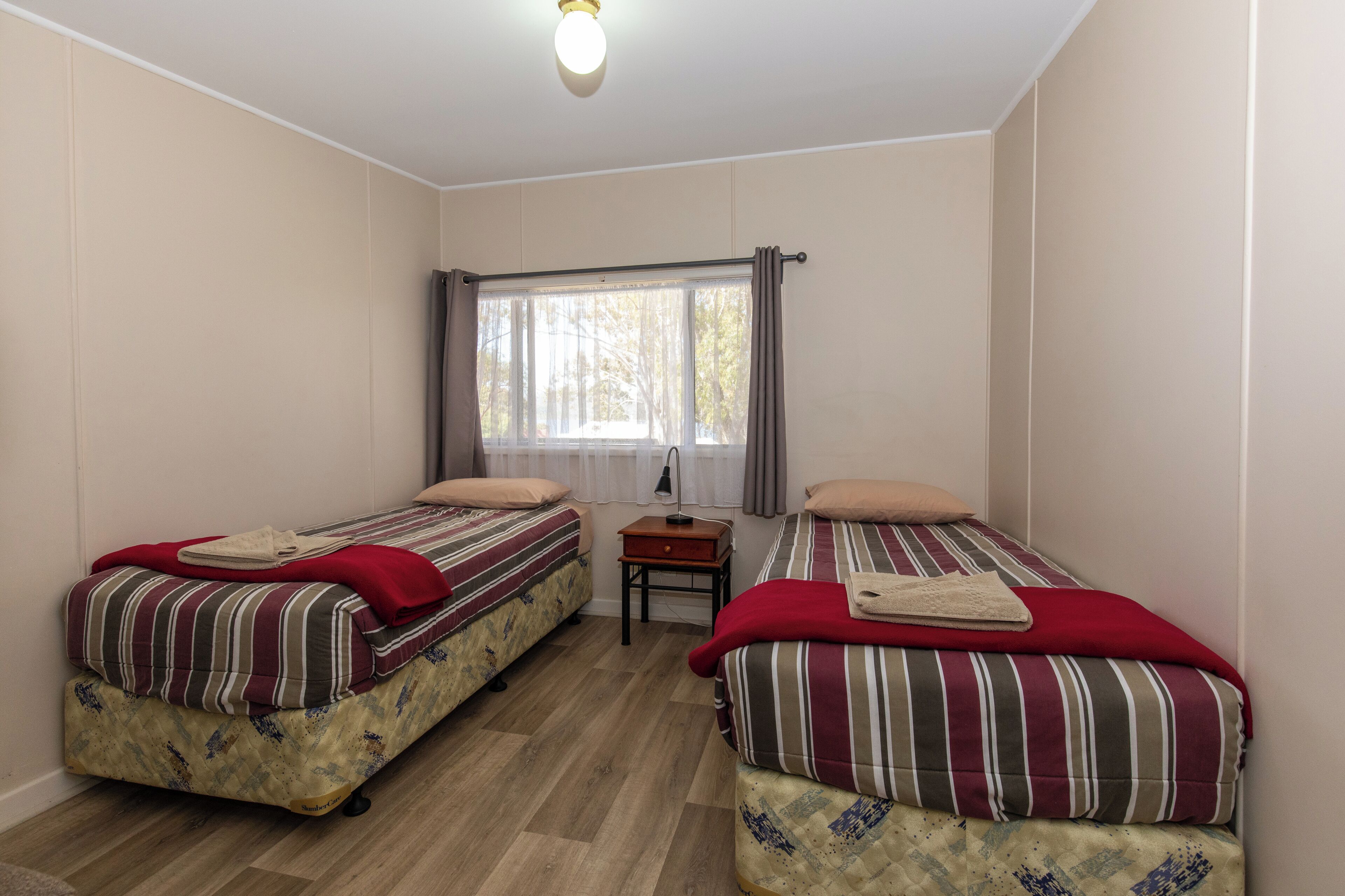 Una habitación con dos camas, cada una con ropa de cama y almohadas a rayas, una mesita con una lámpara y una ventana con cortinas.
