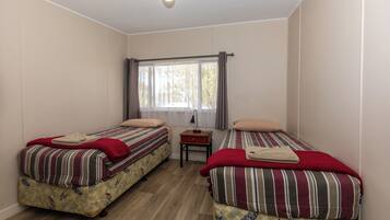 Una habitación con dos camas, cada una con ropa de cama y almohadas a rayas, una mesita con una lámpara y una ventana con cortinas.