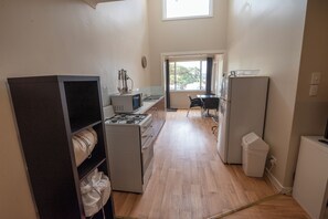 A compact kitchen with a stove, sink, and refrigerator. There is a window providing natural light and a view of the outdoors.