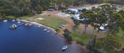 An aerial view of a lakeside property with a dock, boats, and a building with a swimming pool.