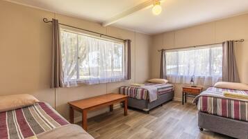 A room with two beds, a bench, a nightstand, and large windows with curtains.