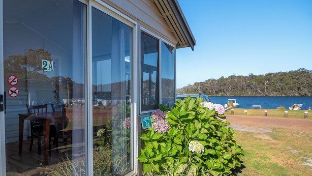 A building with large glass windows, a sign indicating 'Unit 2A', and a view of a lake with boats. - Walpole Rest Point Caravan Park (Walpole)