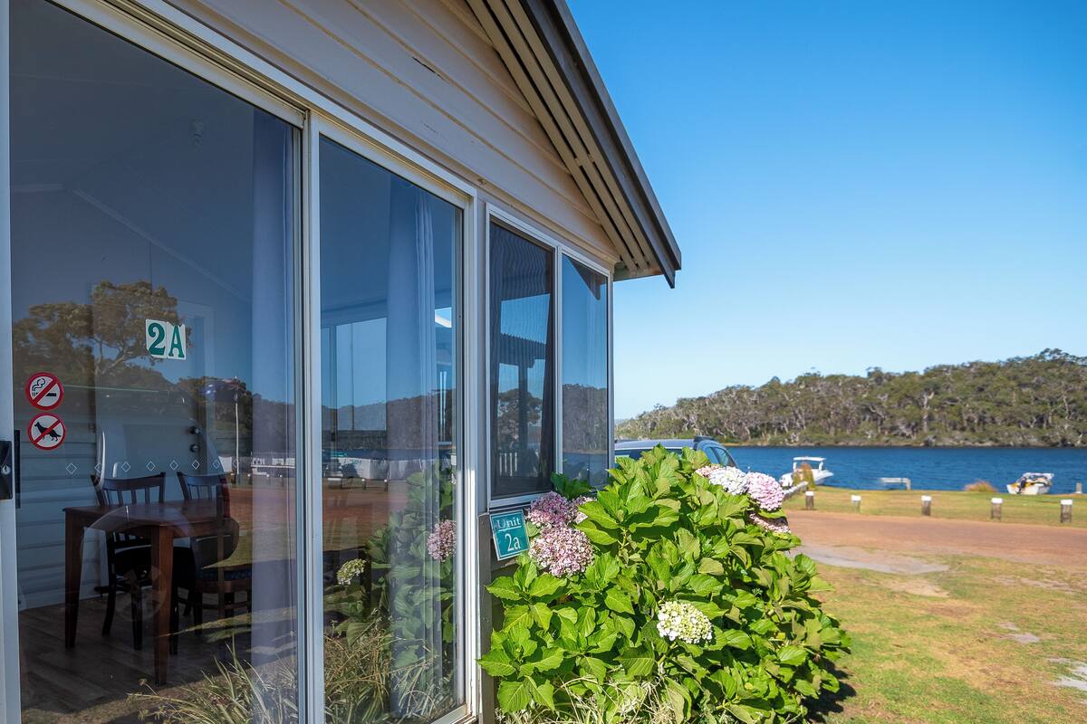 A building with large glass windows, a sign indicating 'Unit 2A', and a view of a lake with boats.