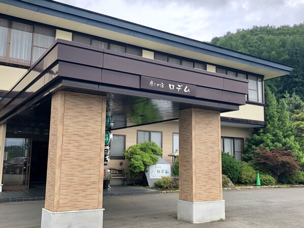 A hotel entrance with a covered walkway supported by wooden pillars, a signboard, and a bench outside.