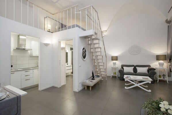A modern living space with a kitchen, dining area, and a staircase leading to an upper level.