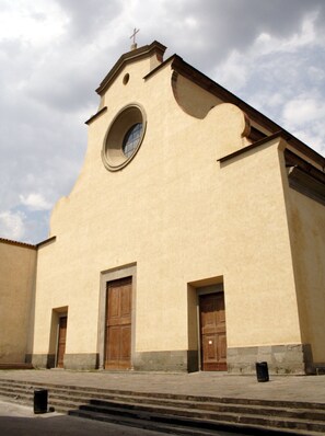 Una iglesia con una ventana circular, dos puertas de madera y una cruz en la parte superior.