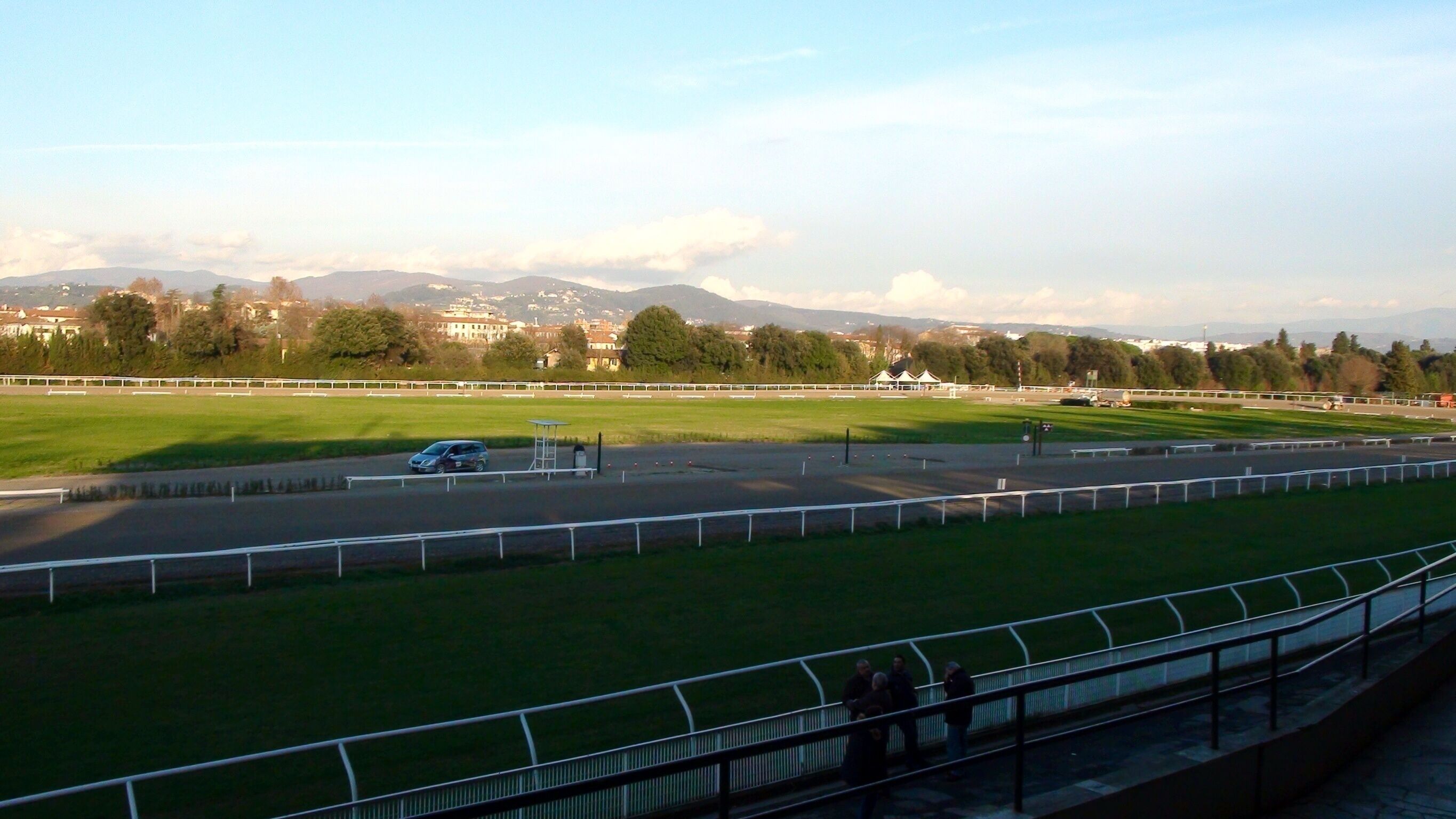 A view of a racecourse with a green field, a track, and a distant mountain range.