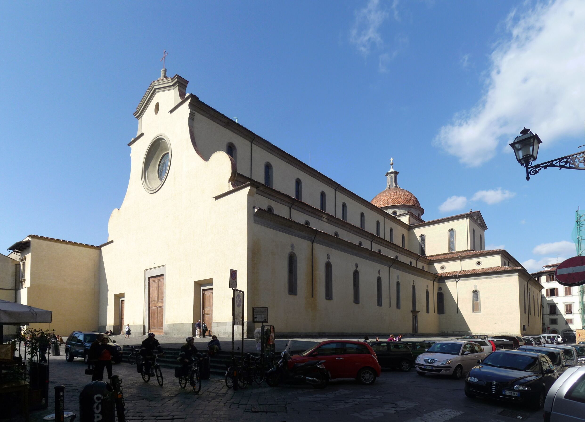 Une église dotée d’un dôme et d’un clocher, entourée de voitures et de vélos garés.