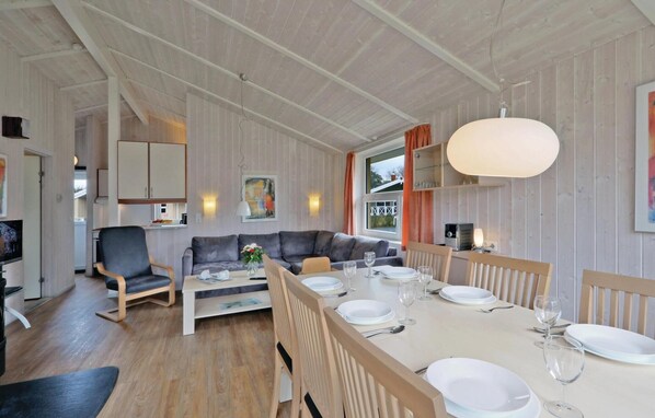 Un espace de repas moderne avec une longue table dressée pour quatre personnes, un canapé et un téléviseur en arrière-plan.