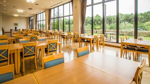 Un vaste espace dédié à la salle à manger, avec de nombreuses tables et chaises, et de grandes fenêtres donnant sur un paysage verdoyant.