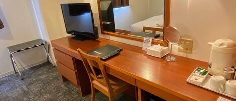 A hotel room with a wooden desk, a television, a mirror, a coffee maker, and a small tray with cups and a remote control.