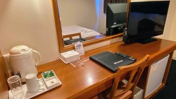 Escritorio de habitación de hotel con cafetera, bandeja con taza y té, control remoto y libreta.