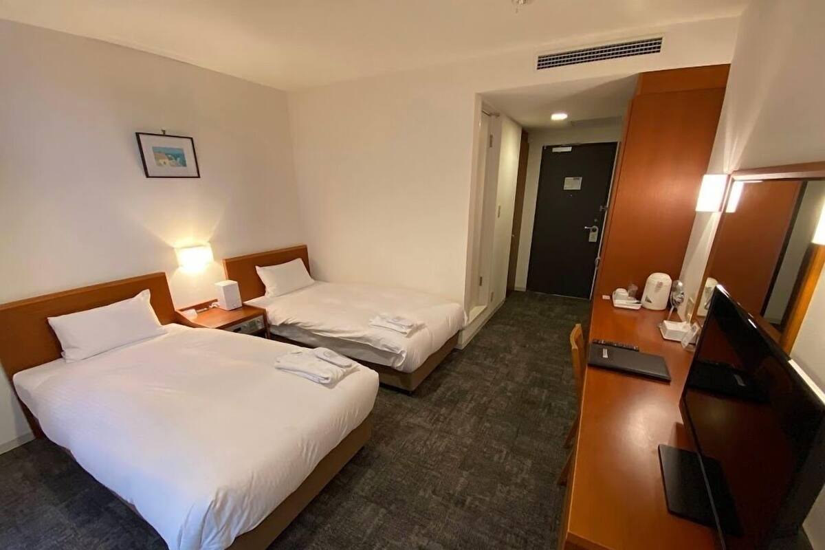 A hotel room with two beds, a desk with a computer, a TV, and a picture on the wall.