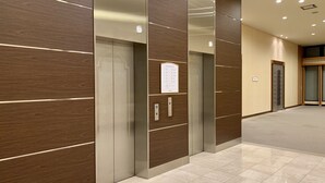 Un espace moderne pour les ascenseurs, avec un lambris en bois et un sol carrelé aux lignes épurées.