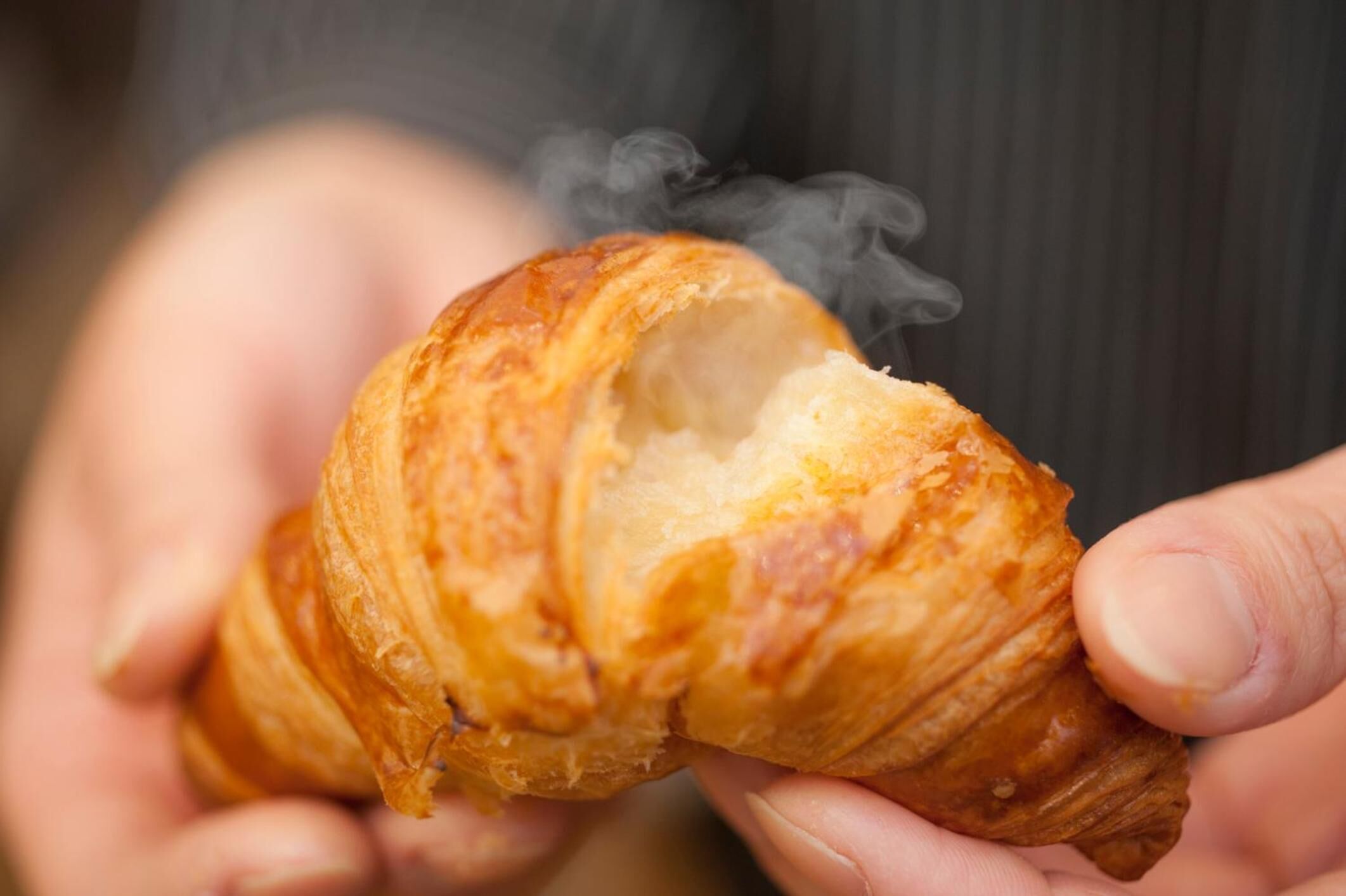 A person holding a croissant with steam rising from it.