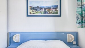A bedroom with a blue headboard, a white bedspread, and a framed landscape painting above the bed. - Beachside Apartment with Pool and Terrace in Urrugne (Urrugne)