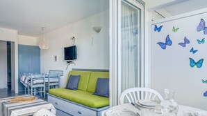 A modern, well-lit room with a green sofa, white chairs, and a dining table set for four. A television is mounted on the wall, and butterfly decals adorn the wall. - Beachside Apartment with Pool and Terrace in Urrugne (Urrugne)