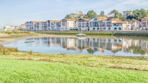 A waterfront hotel with multiple balconies, a reflection pool, and a small boat docked near the shore. - Beachside Apartment with Pool and Terrace in Urrugne (Urrugne)