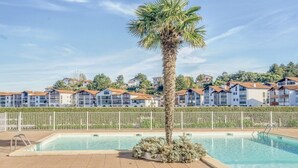 A swimming pool with a palm tree, surrounded by a fence, and buildings in the background. - Beachside Apartment with Pool and Terrace in Urrugne (Urrugne)