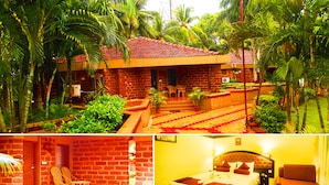 A hotel with a brick exterior, a red-tiled roof, and a garden with palm trees. - Toshali Sands Nature Escape (Puri)